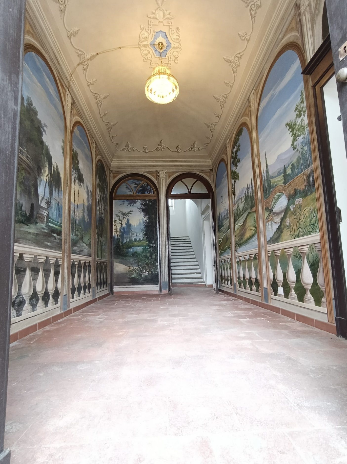 Il corridoio con gli affreschi di paesaggio e il lampadario